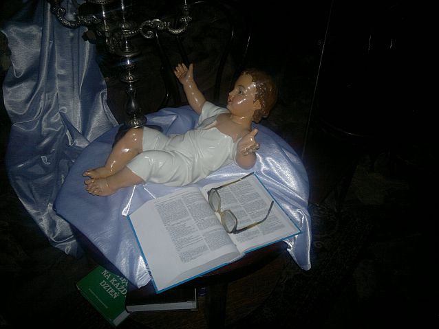 Figurka małego Jezusa, obok otwarta Biblia, na której leżą okulary