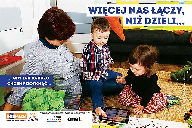 Dziewczynka i chłopczyk bawią się tabletem. Chłopczyk dotyka ekranu stopą, ponieważ nie ma rączek. Hasło: Więcej nas łączy, niż dzieli... gdy tak bardzo chcemy dotknąć...