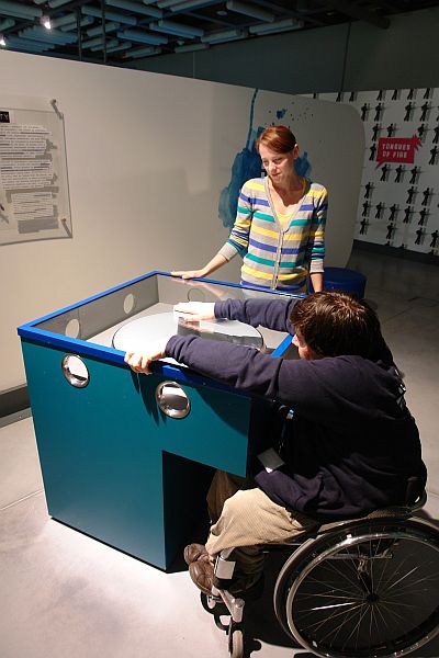 Mężczyzna na wózku przy gablocie z urządzeniem w kształcie okręgu w Centrum Nauki Kopernik
