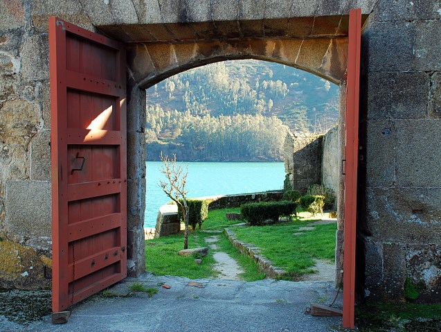 otwarte drzwi w murze, gdzie widać jezioro i góry