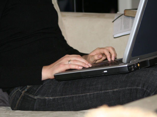 fragment dziewczyny, która trzyma laptop na kolanach i coś na nim pisze