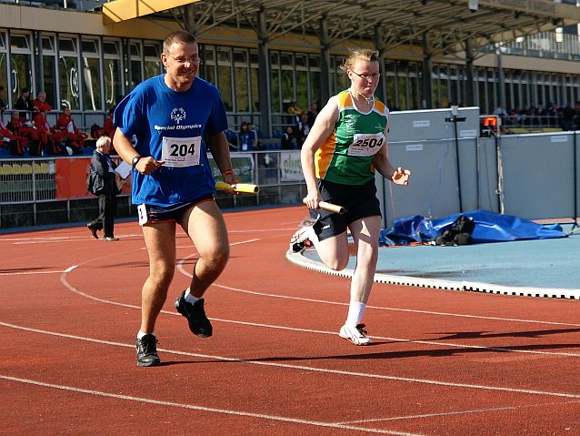 Dwoje zawodników - mężczyzna i kobieta - biegną po bieżni trzymając pałeczki