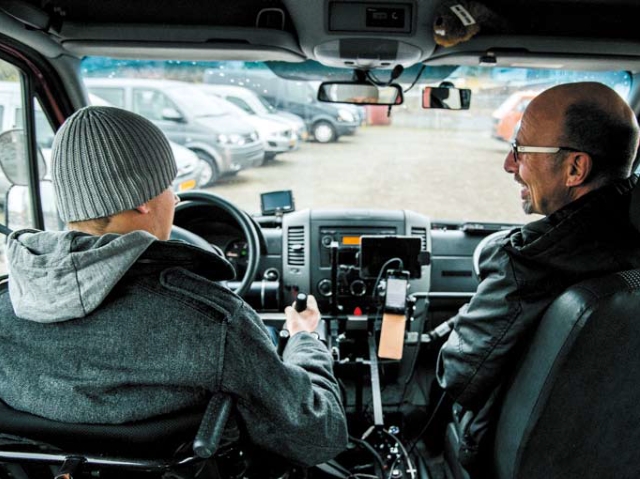 zdjęcie zrobione z perspektywy pasażera z tyłu. widać plecy kierowcy w dostosowanym samochodzie i obok instruktora 