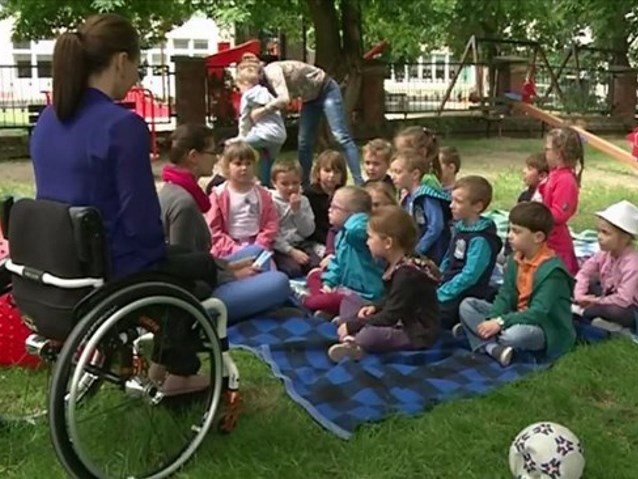kobieta na wózku przed dziećmi, siedzącymi na trawie