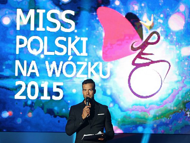 Conrado Moreno stoi z mikrofonem. W tle napis Miss Polski na Wózku 2015