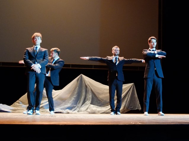 czterech mężczyzn w garniturach stoi na scenie i wykonuje jakiś układ