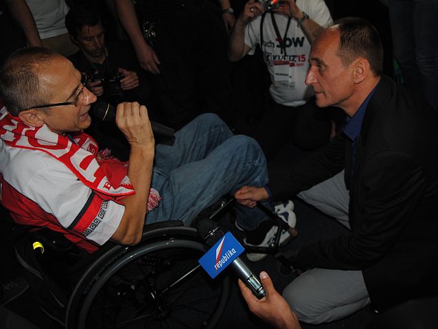 Siedzący na wózku Mirosław Piesak rozmawia otoczony przez dziennikarzy z Pawłem Kukizem