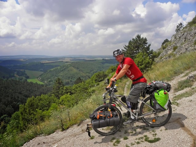Rafał Gręźlikowski stoi rowerem na górce, w tle widok górski