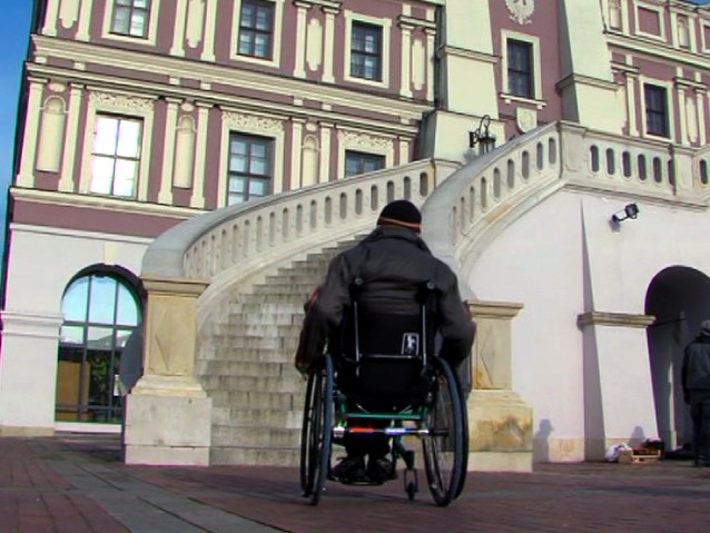 mężczyzna na wózku przed schodami prowadzącymi do ratusza w Zamościu