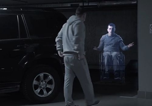 Mężczyzna wysiada z samochodu i ze zdziwieniem patrzy na hologram człowieka na wózku