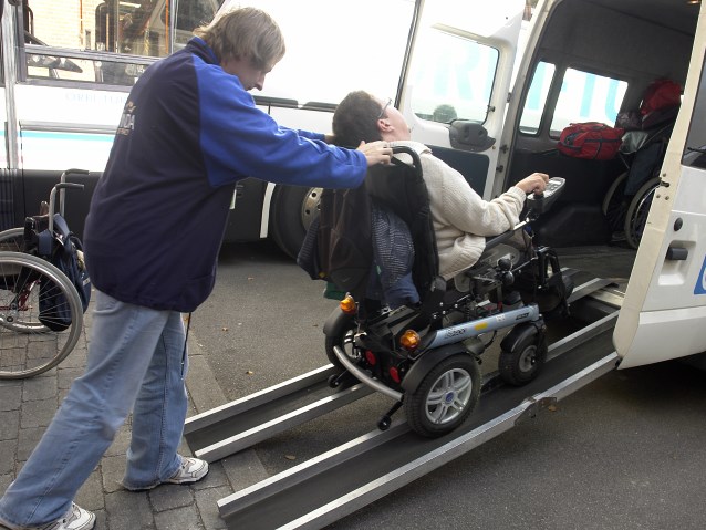 chłopak na wózku inwalidzkim wjeżdża z pomocą do busa