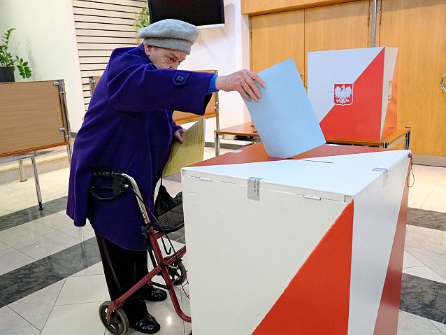 Starsza kobieta z chodzikiem wrzuca głos do urny