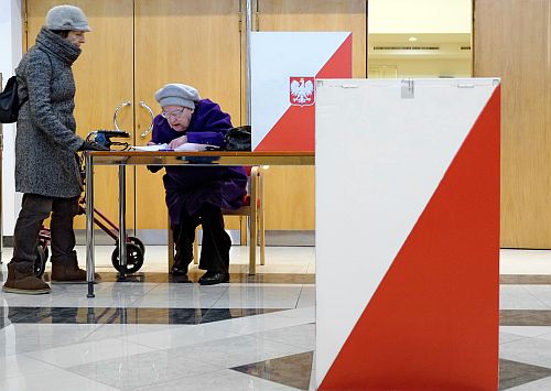 Kobieta pomaga starszej pani oddać głos w lokalu wyborczym