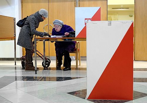 Kobieta pomaga starszej pani wypełniać kartę do głosowania w lokalu wyborczym
