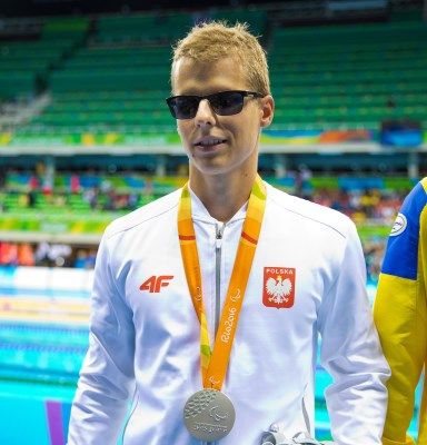Wojciech Makowski w dresie reprezentacji Polski z wiszącym na szyi srebrnym medalem, stoi na tle basenu w Rio
