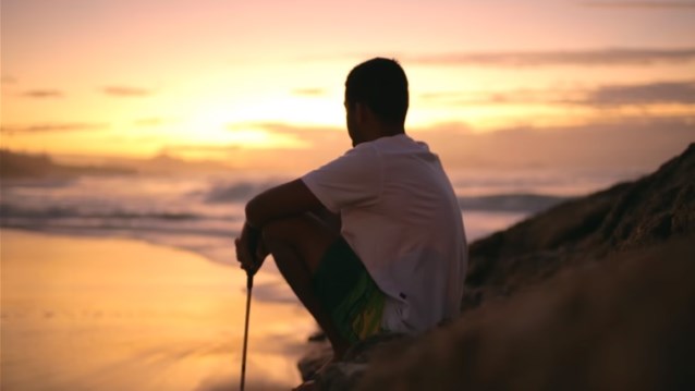 Derek Rabelo siedzi na skale, w tle zachód słońca nad oceanem
