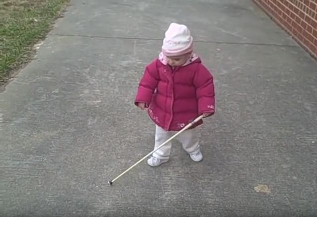 Mała dziewczynka idzie chodnikiem trzymając przed sobą białą laskę