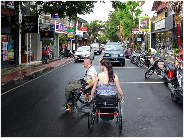 Kobieta i mężczyzna na wózkach na ulicy miasta, którą pędzą samochody