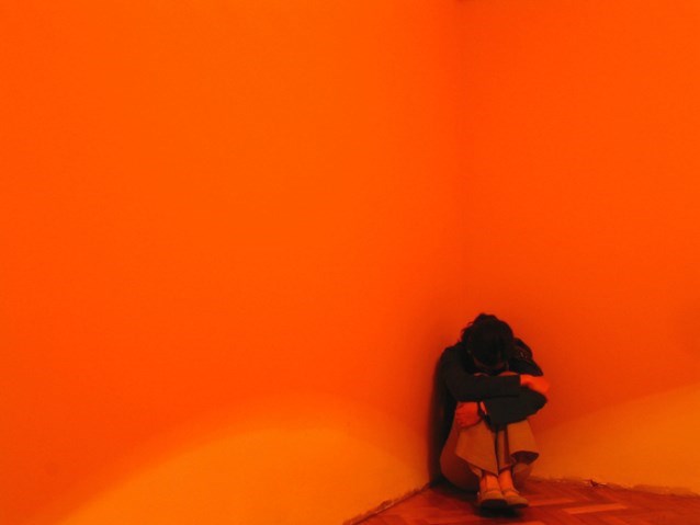 skulona kobieta siedzi w kącie pomarańczowego pokoju