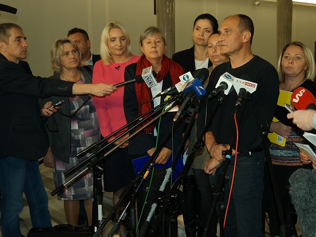 Paweł Kukiz wraz z matkami osób z niepełnosprawnością stoją na korytarzu sejmowym przed mikrofonami dziennikarzy