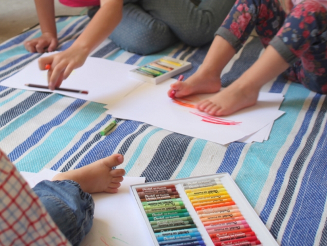 trójka dzieci maluje pastelami kolorowymi, dwoje z nich maluje stopami, a jedno dłońmi