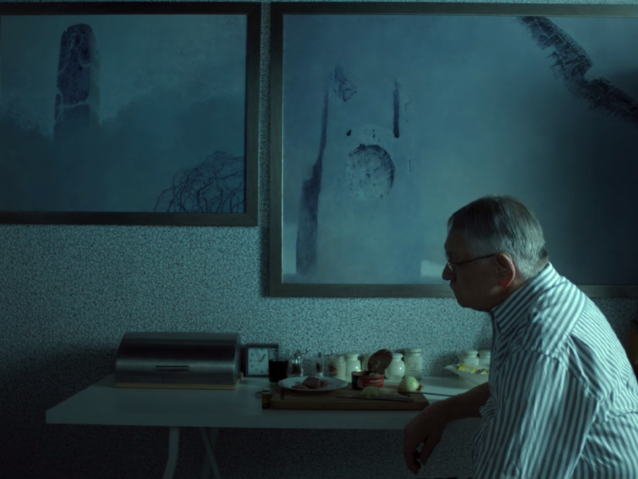 Beksiński (Andrzej Seweryn) siedzi przy stole. Na ścianie wiszą jego dwa obrazy