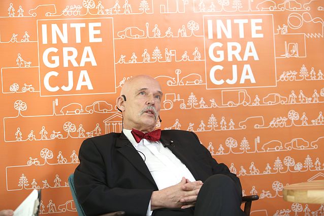 Janusz Korwin-Mikke siedzi w tle z banerem Integracji