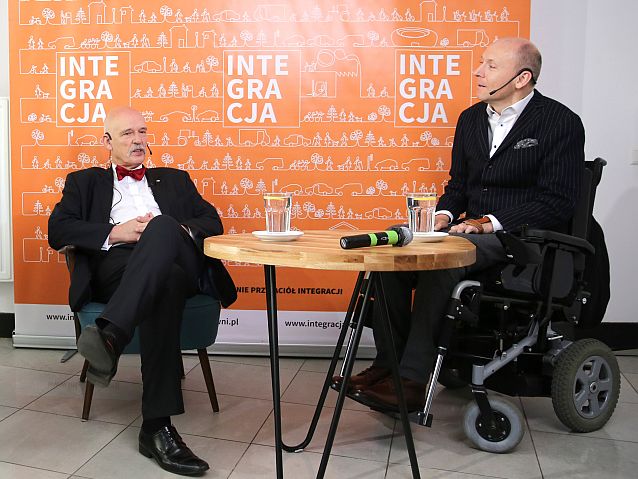 Przy stoliku siedzą i rozmawiają Janusz Korwin-Mikke i Piotr Pawłowski