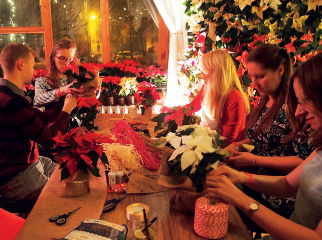 kilka osób siedzi przy długim stole i wykonuje ozdoby świąteczne