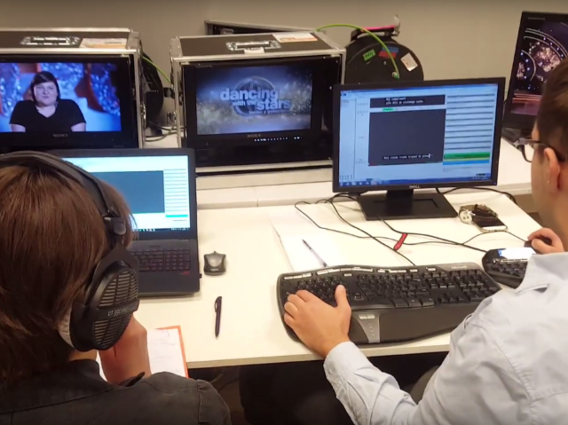 dwie osoby siedzą przed pięcioma monitorami i robią napisy dla niesłyszących