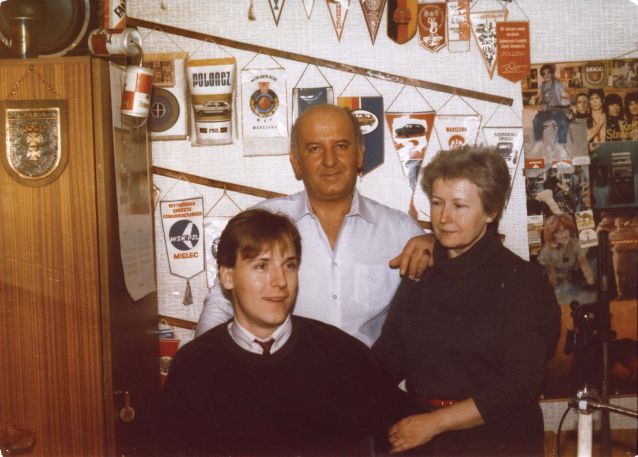 Piotr Pawłowski ze swoimi rodzicami w mieszkaniu, na ścianie wiszą proporczyki, plakaty