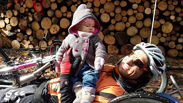 Rafał Szumiec leży na rowerze ręcznym trzymając córeczkę