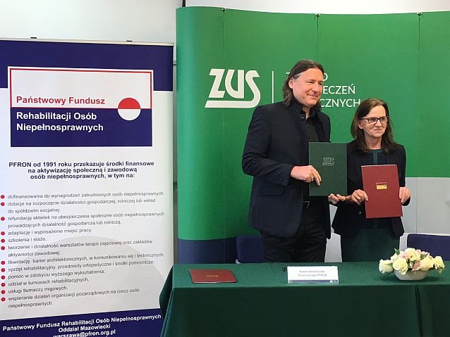 Prof. Gertruda Uścińska i Robert Kwiatkowski stoją z teczkami za stołem na tle banerów PFRON i ZUS