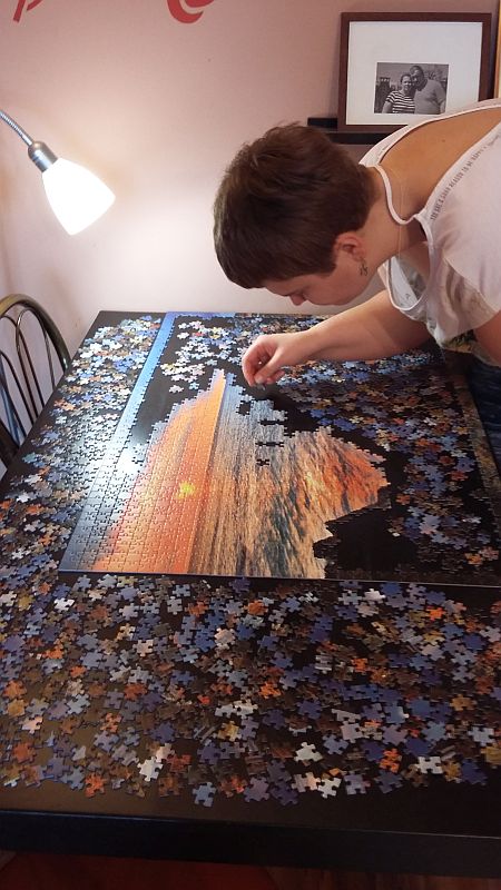 Młoda kobieta układa na stole duże puzzle
