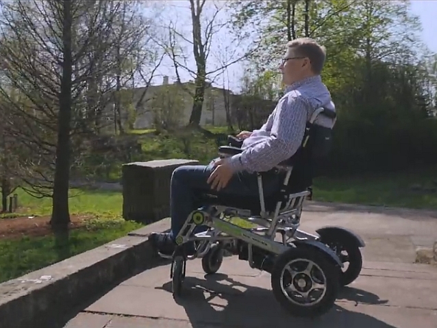 Mężczyzna na wózku elektrycznym stoi w parku na mostku
