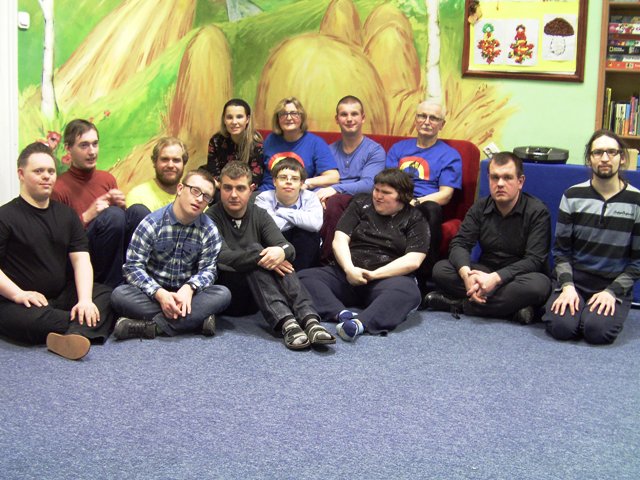 dziesięciu młodych mężczyzn z zespołem Downa i spektrum autyzmu siedzą na podłogach, obok nich terapeuci