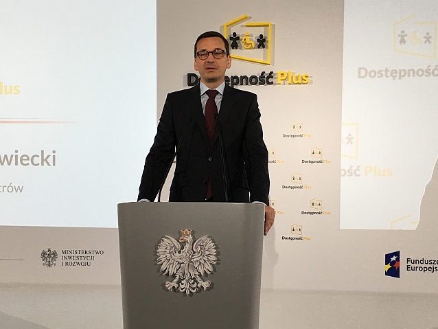 Premier Mateusz Morawiecki podczas przemówienia stoi przy mównicy. Za nim napis: Dostępność plus