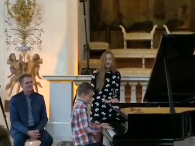 Igor Sobierajski gra na fortepianie, obok niego śpiewa dziewczyna