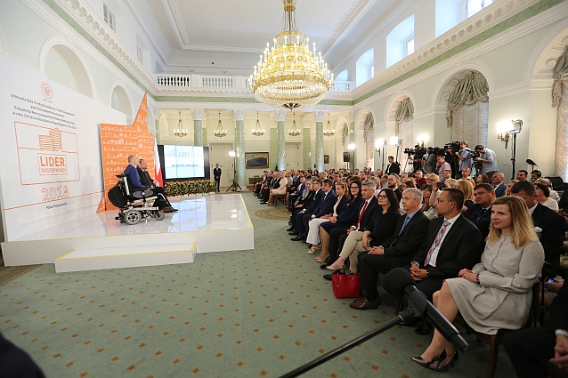 Elegancka sala w Pałacu Prezydenckim. Po lewej podest z prowadzącymi galę, po prawej siedząca na krzesłach publiczność