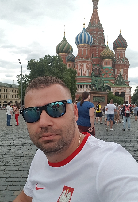 Mężczyzna pozuje do zdjęcia na placu Czerwonym, w tle bogato zdobiona, kolorowa cerkiew