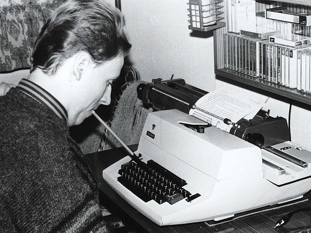 Piotr Pawłowski siedzi w mieszkaniu nad maszyną do pisania i stuka w klawisze trzymanym w ustach patyczkiem