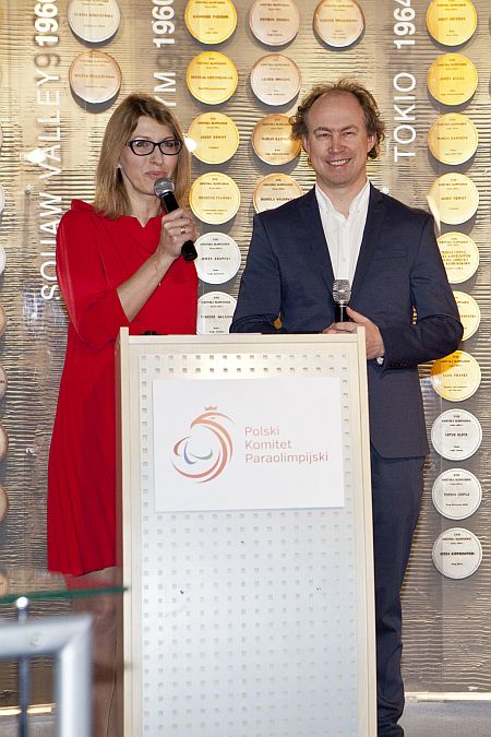 Za mównica stoją Paulina Malinowska-Kowalczyk - z mikrofonem - oraz Michał Pol. W tle ściana z symbolicznymi medalami naszych olimpijczyków