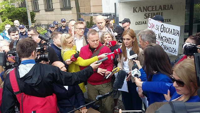Monika Zima-Parjaszewska przemawia, otoczona wianuszkiem dziennikarzy i protestujących