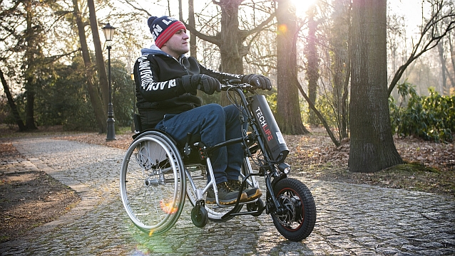 Mężczyzna na wózku ręcznym jedzie przez park z podłączonym z przodu wózka napędem