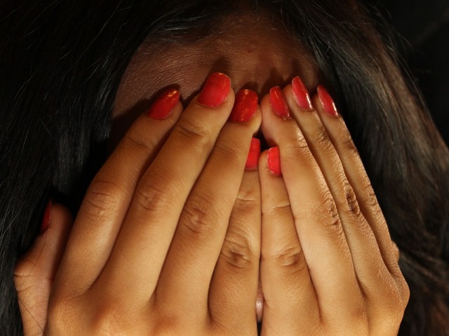 Kobieta zasłania twarz dłońmi, ma długie czerwone paznokcie
