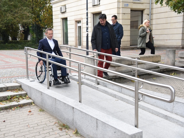 Przed siedzibą Integracji Paweł Rabiej siedzi na wózku, zjeżdża powoli z podjazdu. Obok niego po schodach idzie asekurant