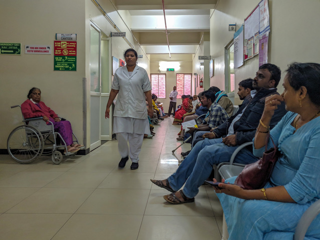 Szpital w Bengaluru, ludzie siedzą pod ścianą na krzesłach w poczekalni