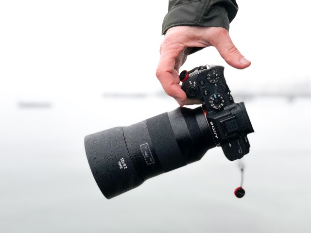 męska ręka trzyma aparat fotograficzny z długim obiektywem