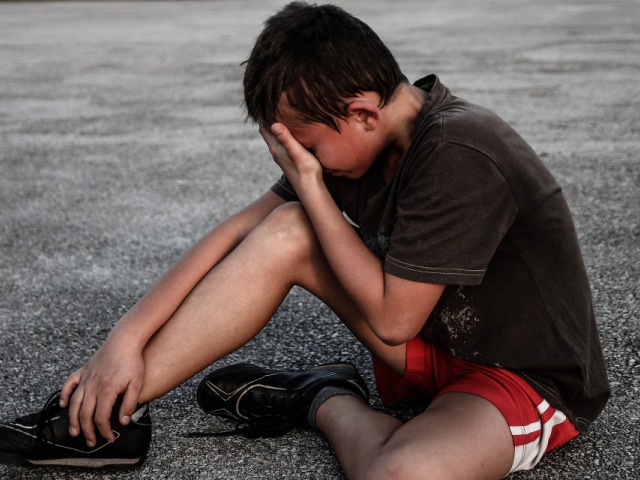chłopiec nastolatek siedzi na chodniku z ręką którą zakrywa twarz