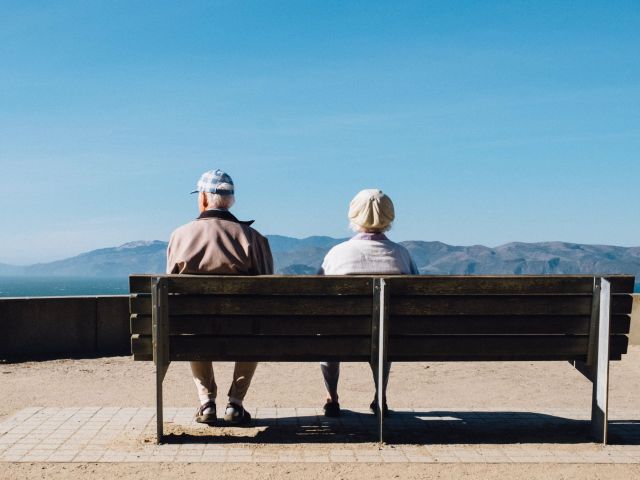Starsza pani i pań siedzą tyłem na ławce z widokiem na góry